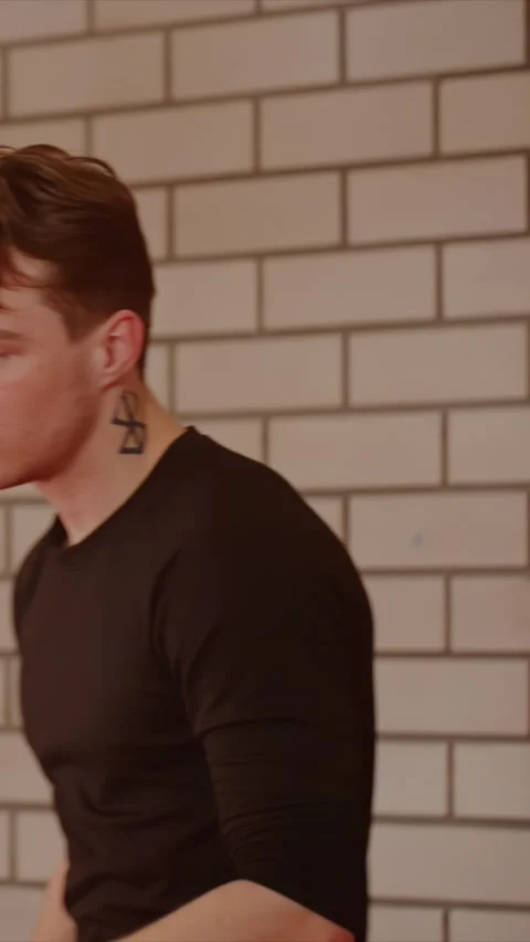 Young man with neck tattoo prepares for boxing against beige brick wall with Stock Footage 343094328