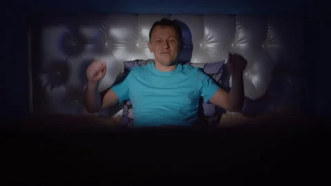 A young man at night lying on a bed watching a music program and dancing with Stock Footage 132708380