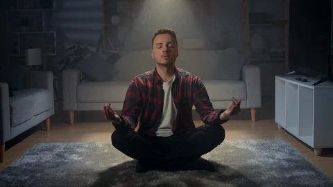 A young man at night relaxes at home on the floor in a lotus position. A warm Stock Footage
