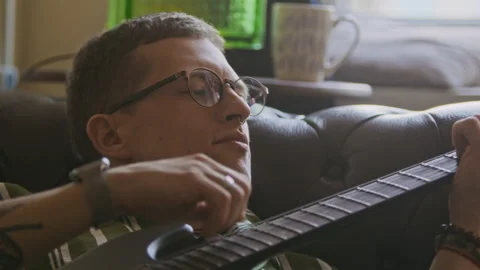 Young Man with Nose Piercing Strumming Electric Guitar on Home Sofa Stock Footage 334797259