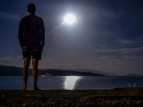 A young man observing the moonlight reflection in the surface of the sea in K Stock Photos