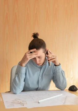 Young man in office with headache while talking on the phone Foto stock