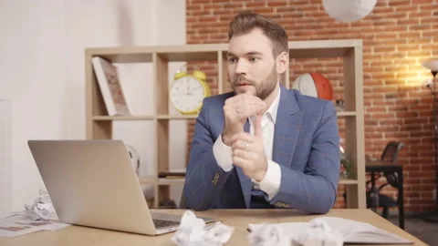 A young man in the office sits at a table and looks around thoughtfully Vidéo 188793453