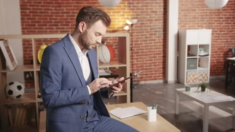 A young man in the office sits on a table and works on a computer tablet Stockbeeldmateriaal 194363435