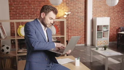 A young man in the office sits on a table and types something into a laptop Stock-Footage 194363498