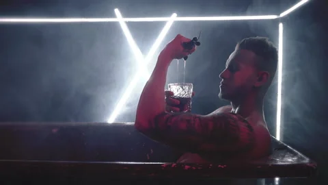 Young man in old bath drinks a drink and pours himself Stock Footage 147633402