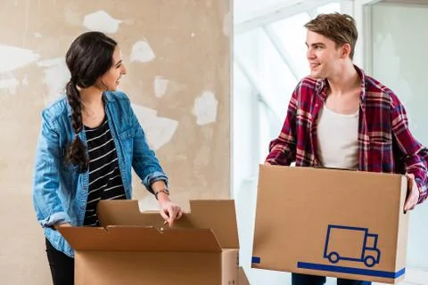 Young man opening a box while moving with his girlfriend into a Stock Photos