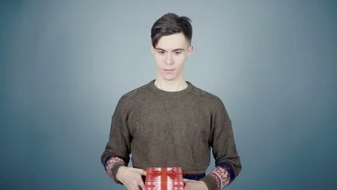 Young man opening a gift box with a surprise pulls out a Santa hat Stock Footage 70223457