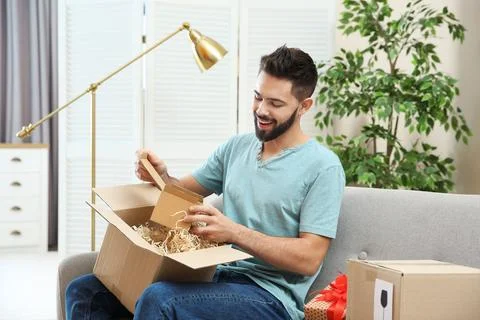 Young man opening parcel on sofa at home Stockfoto's