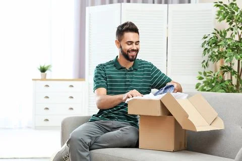 Young man opening parcel on sofa at home Foto stock