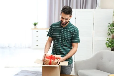 Young man opening parcel on table at home Stock Photos