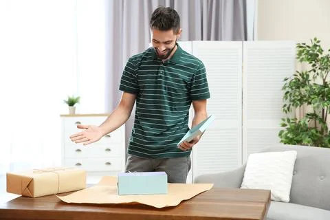 Young man opening parcel on table at home Stock Photos