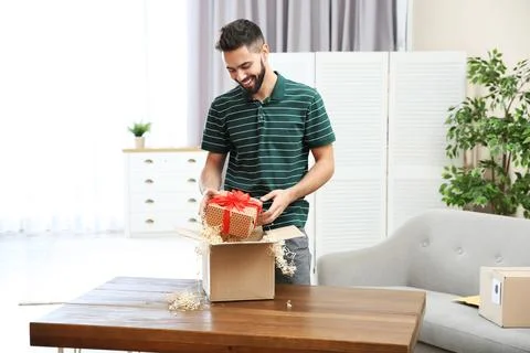 Young man opening parcel on table at home Foto stock
