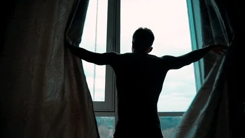 A young man opens the curtains by the window, in the early morning Video stock 104899666