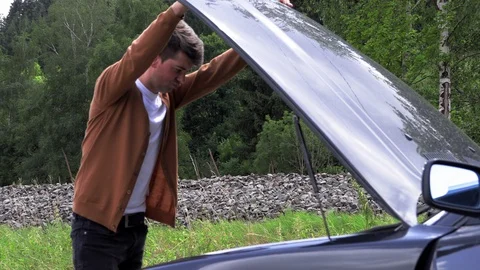 A young man opens the hood of a broken car. 库存影片 113399527