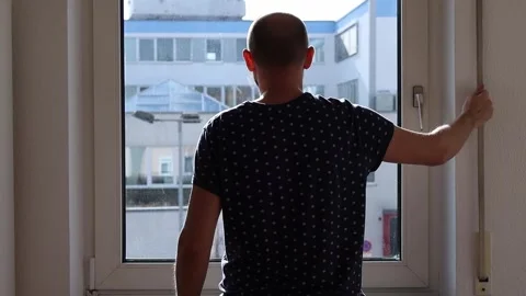 Young man opens the window shutter and looks out the window Stock Footage 242719998