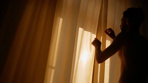 A young man opens the yellow curtains in the room. Sunlight through the curtains Stock Footage 143268796
