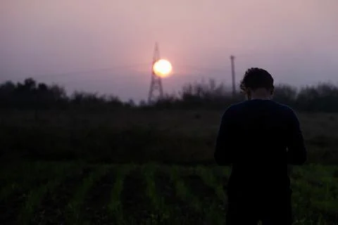 A young man operating camera standing in dark, with beautiful sunset and si.. Stock Photos
