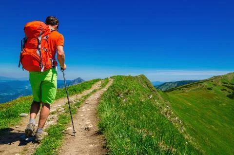 Young man with orange backpack, road and meadows Stock Photos