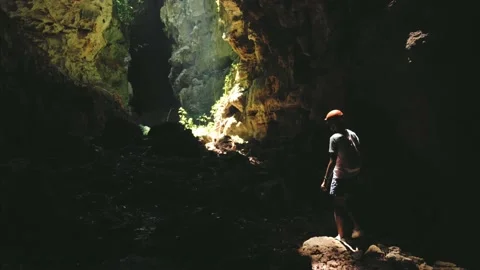 Young man with an orange helmet inside a cave walking at light coming Stock Footage 157896361