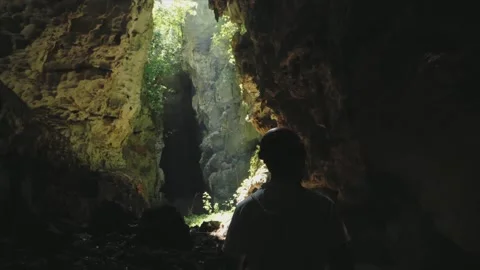 Young man with an orange helmet inside a cave walking at light coming Stock Footage 157896431