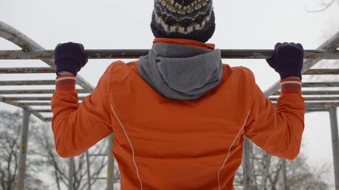 Young man in orange jacket doing pullups on horizontal bars outdoors in winter 스톡 동영상 89421986