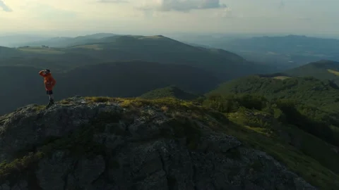 Young man in orange jacket standing at the edge and enjoys success achieved from Stock Footage 158076396