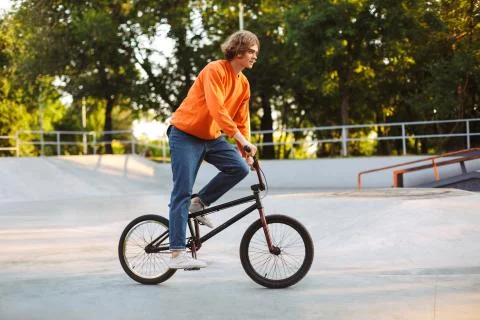 Young man in orange pullover and jeans riding bicycle at skatepark Stock Photos