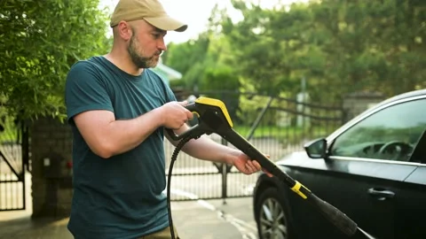 Young man outdoors using a water gun to wash his car Stockbeeldmateriaal 201389788