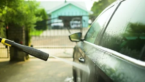 Young man outdoors using a water gun to wash his car Видео 221724067