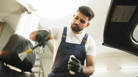Young man in overalls and protective gloves, cleaning car seat with soft brush Stock Footage 233605541