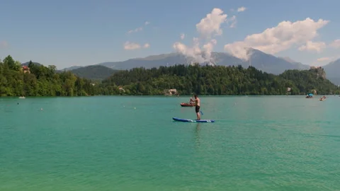 Young man paddleboarding on the turquoise water of Lake Bled Stock Footage 346126370