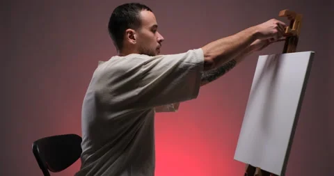 Young man painter placing canvas on easel Stock Footage 233905593