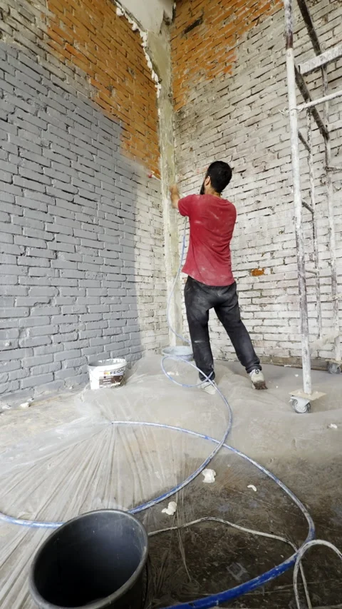 Young man paints old brick wall in grey color with sprayer in apartment Stock Footage 323860735