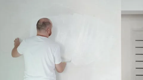 Young man paints the wall with a roller with white Stock Footage 265291587