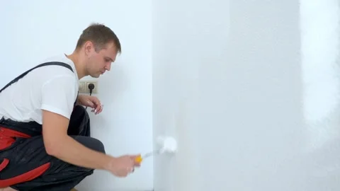 Young man paints the wall in the room with a roller white paint Stock Footage 167185846