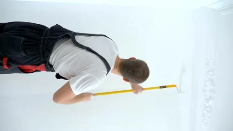 Young man paints the wall in the room with a roller white paint, vertical Stock Footage 167185864