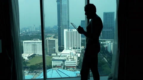 Young man in pants using tablet computer standing by window Stock Footage 55259869