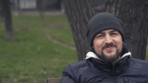 Young man in park drinks coffee. Happy man in hat is resting on bench. Stock Footage 83885650