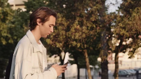 Young man in the park is typing a message.  Guy walks  in the park and typi.. Stock Footage 254657273