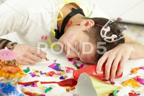 Young man in party hat sleeping on table among confetti and remnants of food Stock Photos