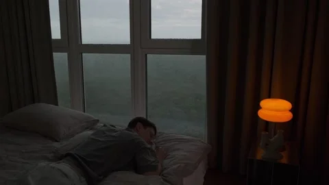 Young man peacefully sleeping on bed near panoramic window while rain falls Stock Footage 312327246