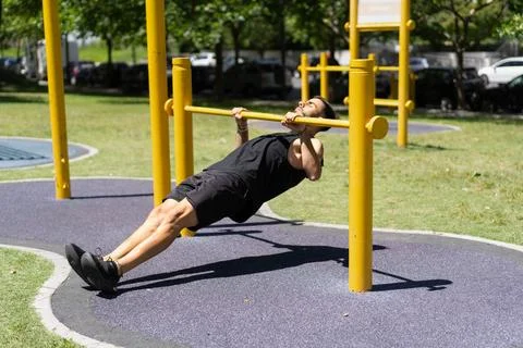 Young man performing inverted rows on outdoor bars Stock Photos