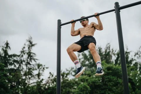 Young man performing pull-ups on metal bars outdoors, demonstrating strength and 库存照片