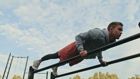 Young Man Performing Push-Ups on Parallel Bars in Outdoor Gym Stock Footage 315175644