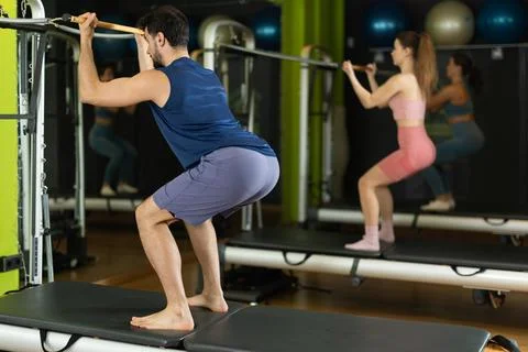 Young man performing squat exercise on pilates reformer in studio Stock Photos