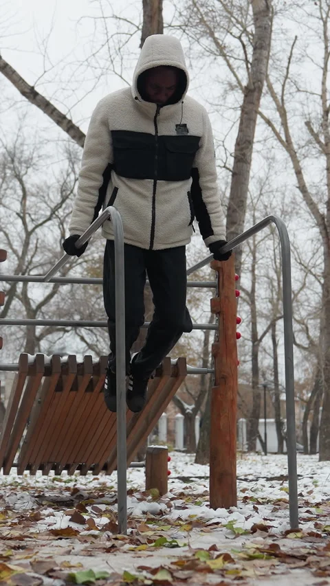 Young Man Performing Strength Training on Parallel Bars in Snowy Urban Park Stock-Footage 318586309