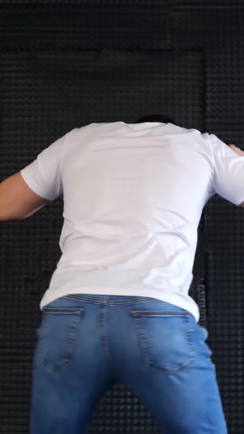 Young Man Performs Energetic Dance Moves Against Dark Textured Studio Wall Stock Footage 347191439