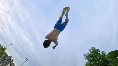 Young man performs impressive backflip into a sparkling blue swimming pool Stock Footage 341243502