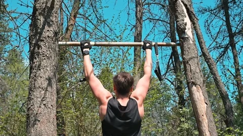 A young man performs pull-ups using a wooden bar set between trees in a forest Video stock 339090253